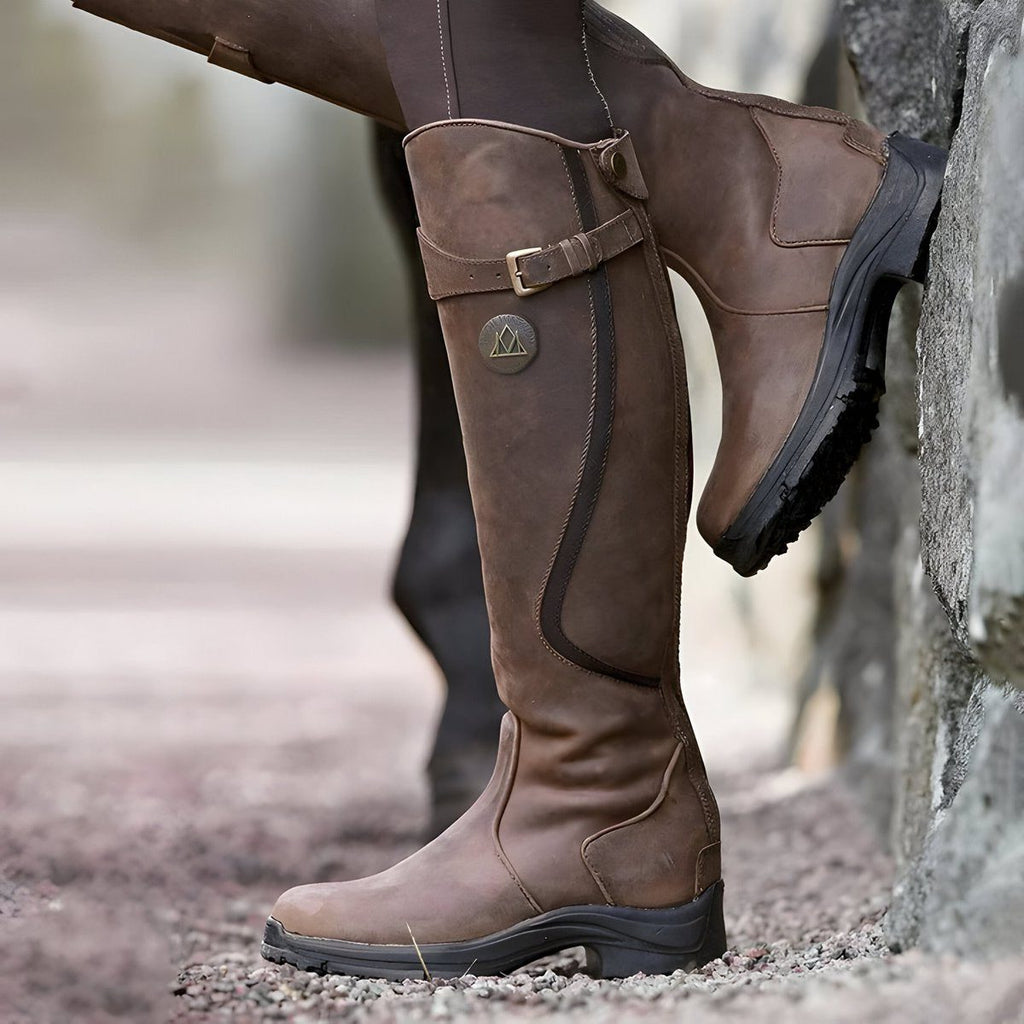 Dark brown tall riding boot standing upright, buckle strap fastened at the shaft