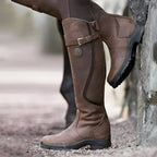 Dark brown tall riding boot standing upright, buckle strap fastened at the shaft